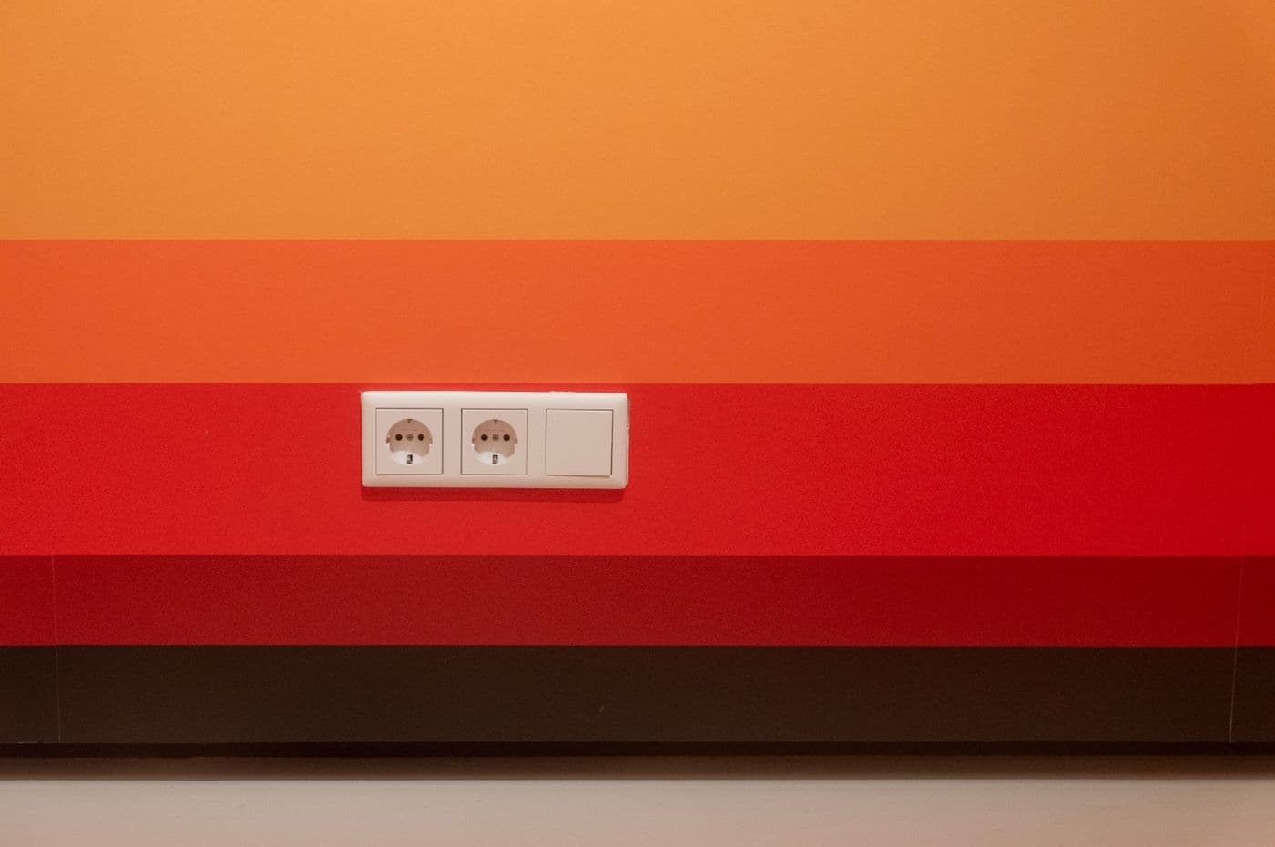 Two electrical sockets on an orange and red striped wall