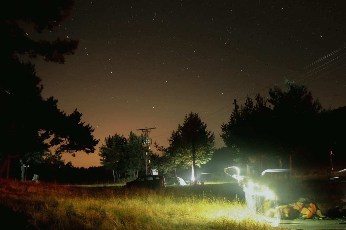 A tent glowing from a lantern inside, pitched among trees after dark