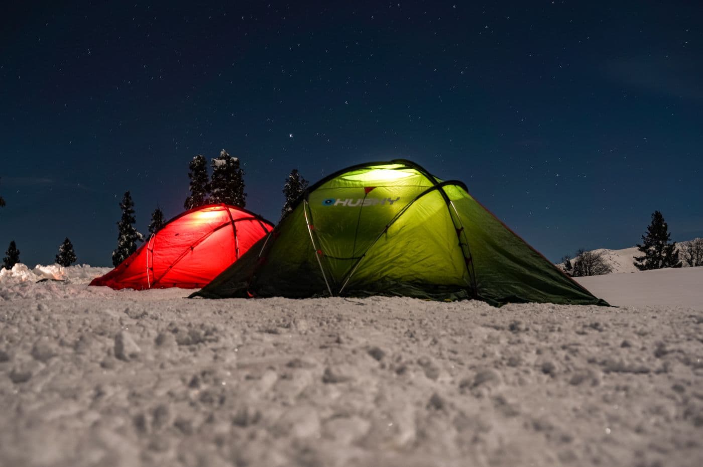 Two lit tents on a snowy landscape under a clear night sky