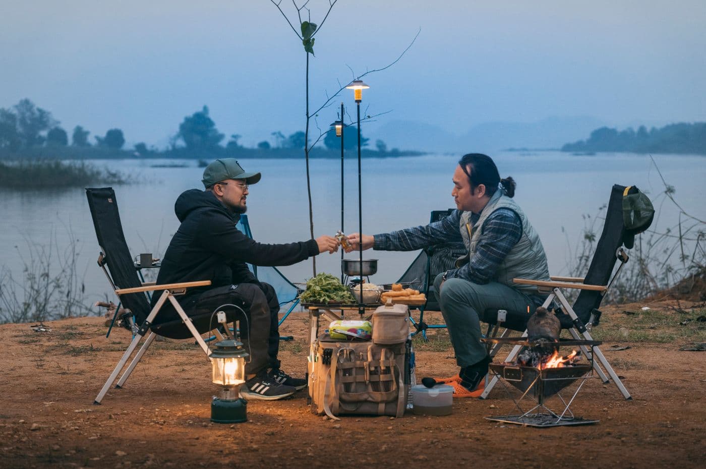 Two people sitting beside a lakeside campfire at dusk