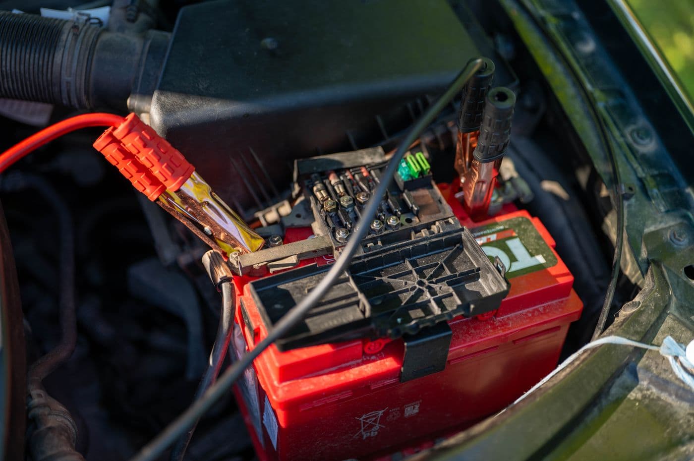 A car battery with red jumper cables attached, photographed close up