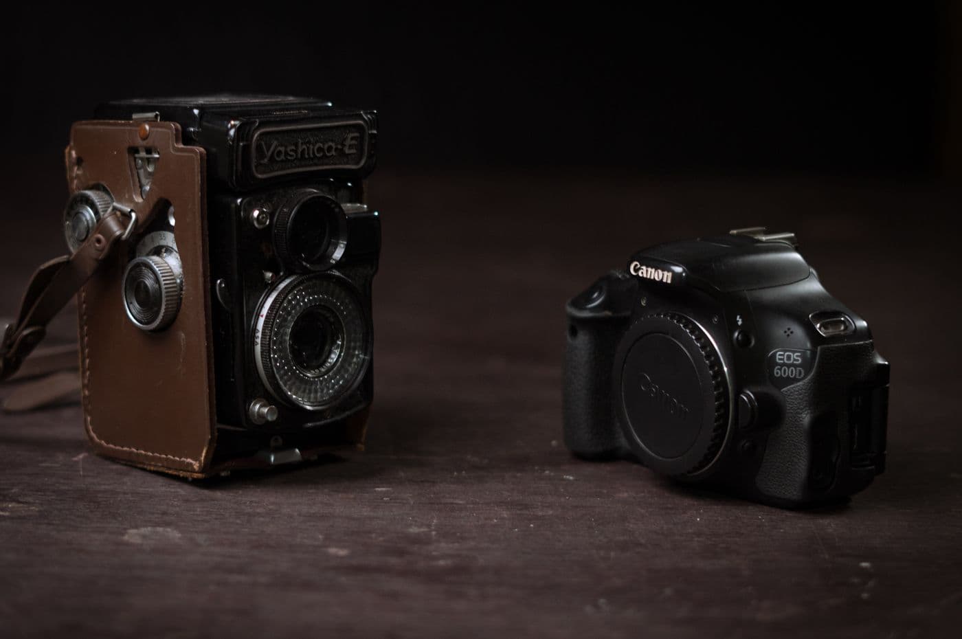 A vintage film camera and a modern DSLR photographed side by side
