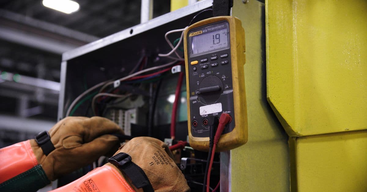 An electrician using a multimeter on a wiring panel