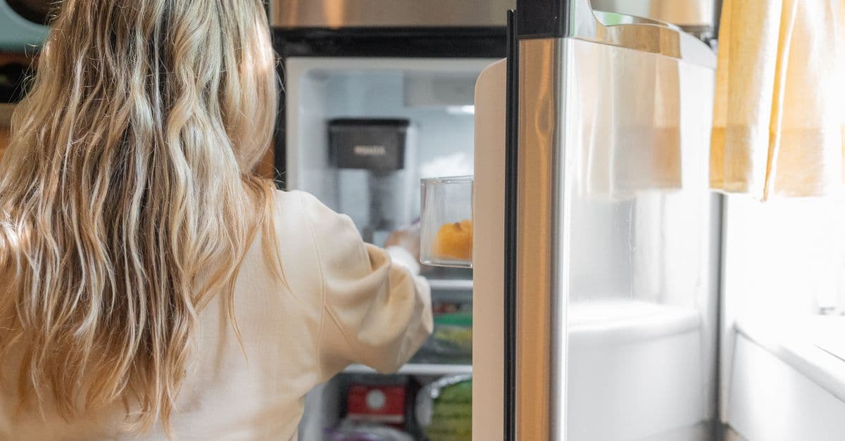 Someone reaching into an open refrigerator in a bright kitchen