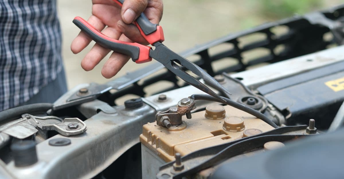 A close-up of someone checking a battery's terminals with pliers