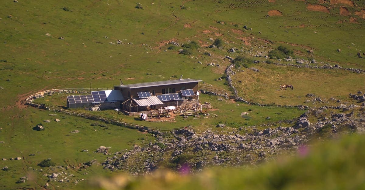 An aerial view of a small cabin with roof solar panels on a green hillside