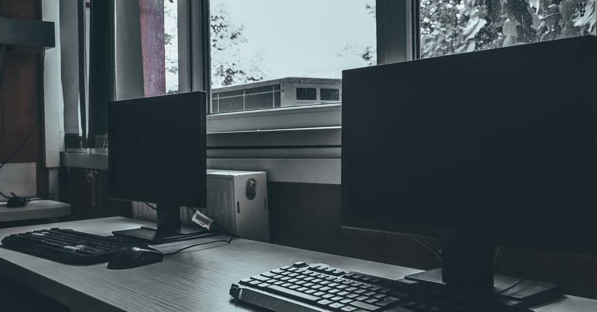 Desktop computers on a desk beside a window